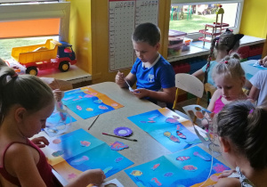 Dzieci naklejają rybki i muszekki na niebieski karton